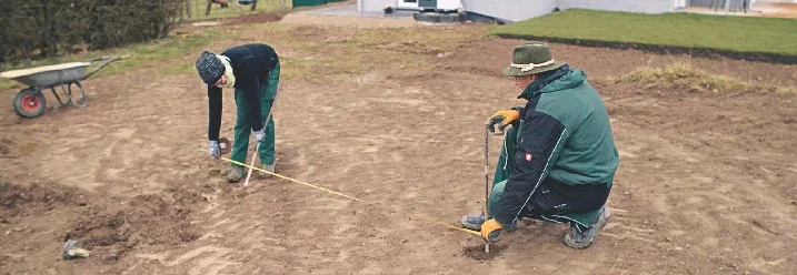 Zwei Personen messen mit einem Maßband den Untergrund aus.
